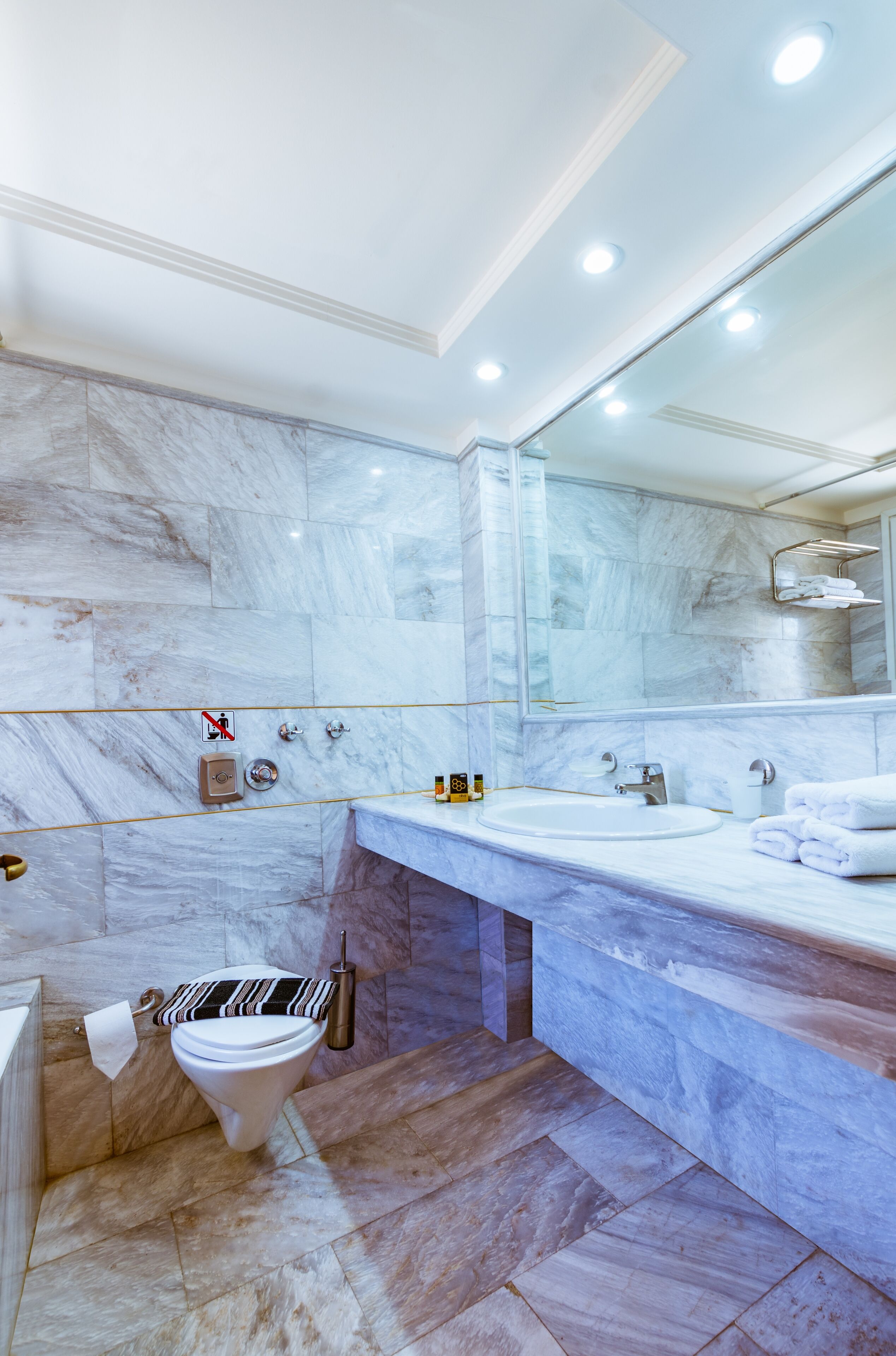 Un baño moderno con azulejos de mármol, un espejo grande, un lavabo y un inodoro.