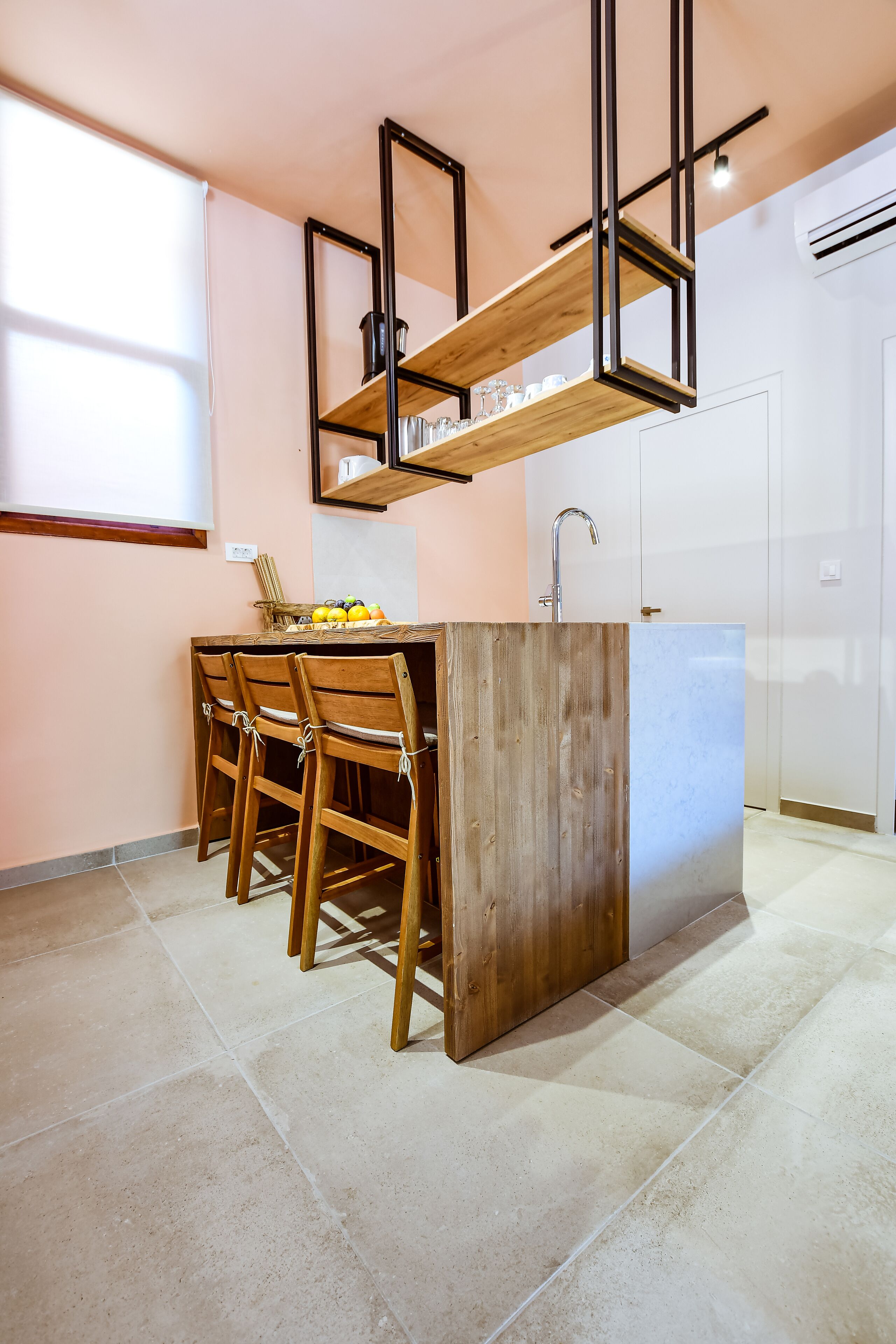 Une cuisine moderne avec un îlot central, des chaises en bois, une étagère intégrée et une porte blanche en arrière-plan.