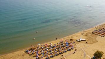 A beach with rows of umbrellas and beach chairs, a sandy shore, and a calm sea.