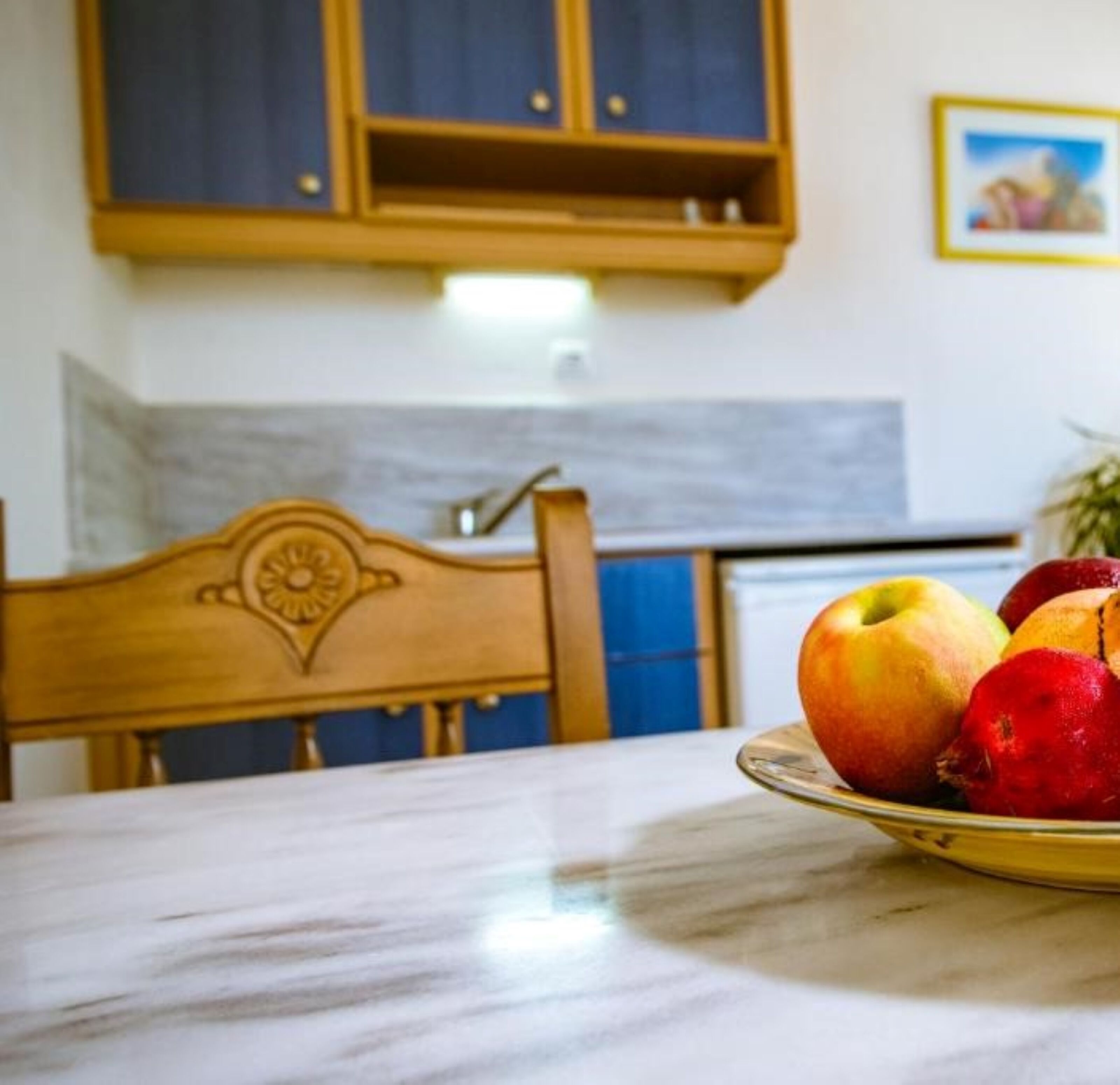 A dining table with a plate of fruit in a room with wooden furniture and a kitchen in the background.
