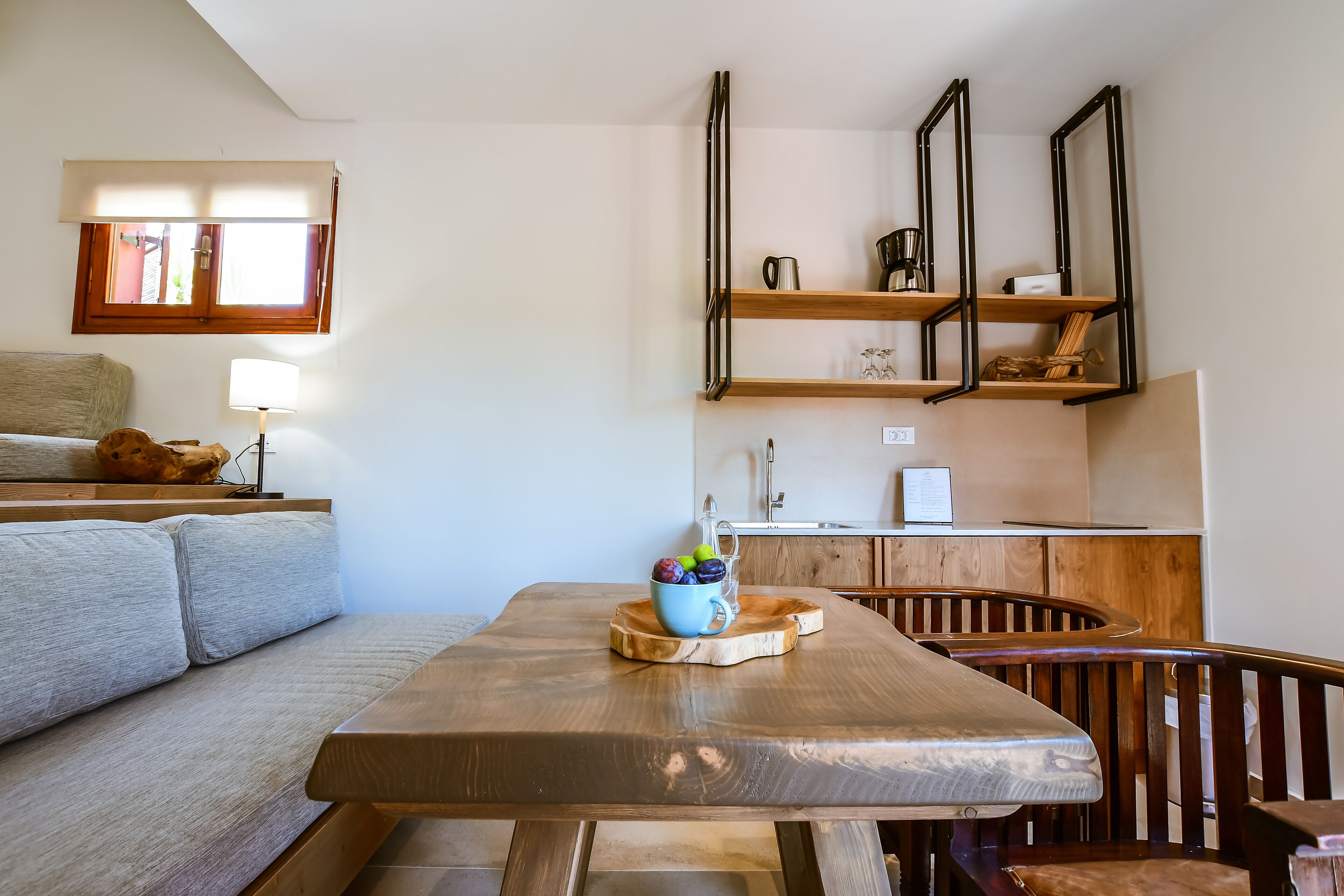 A modern living room with a wooden dining table, a sofa, and a kitchen area with wooden shelves.