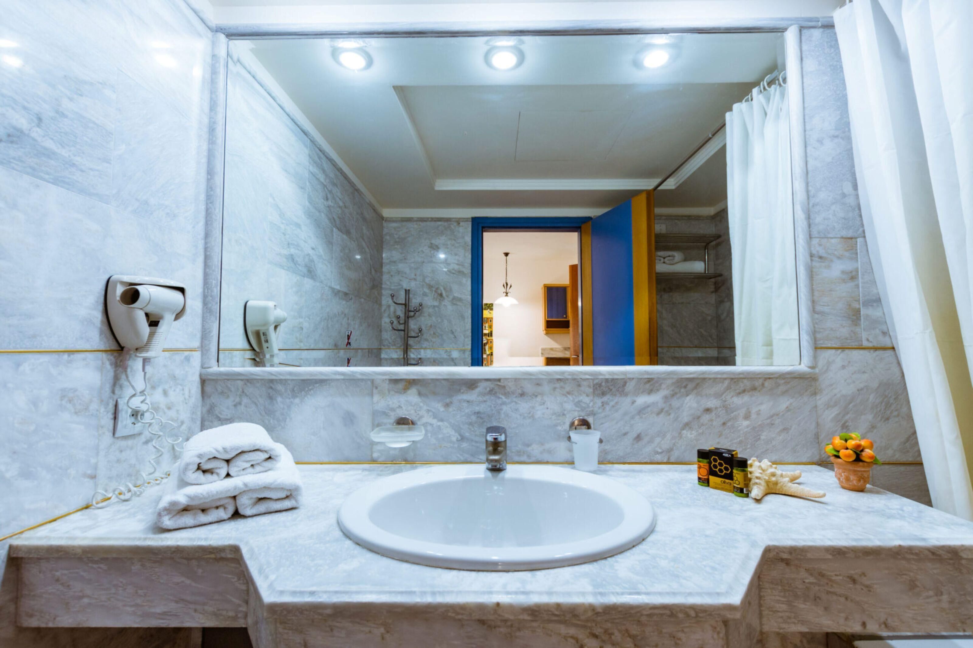 A bathroom with a marble sink, a towel rack, a hand dryer, and a mirror.