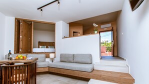 A modern living area with a grey sofa, wooden staircase, and a dining table with fruit. - Anais Collection Hotels & Suites by GHH (Chania)