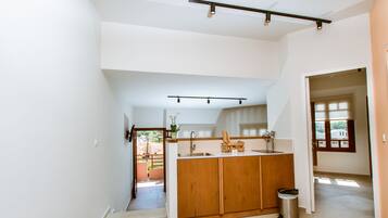 A modern kitchen with wooden cabinets, a countertop, and a sink. There is a trash can and a window providing natural light.