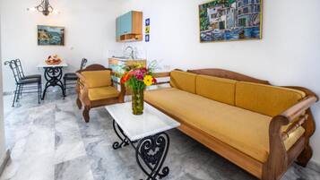 Un salon confortable avec un canapé, une table à manger et des chaises. Un tableau orne le mur et un vase rempli de fleurs est posé sur la table.