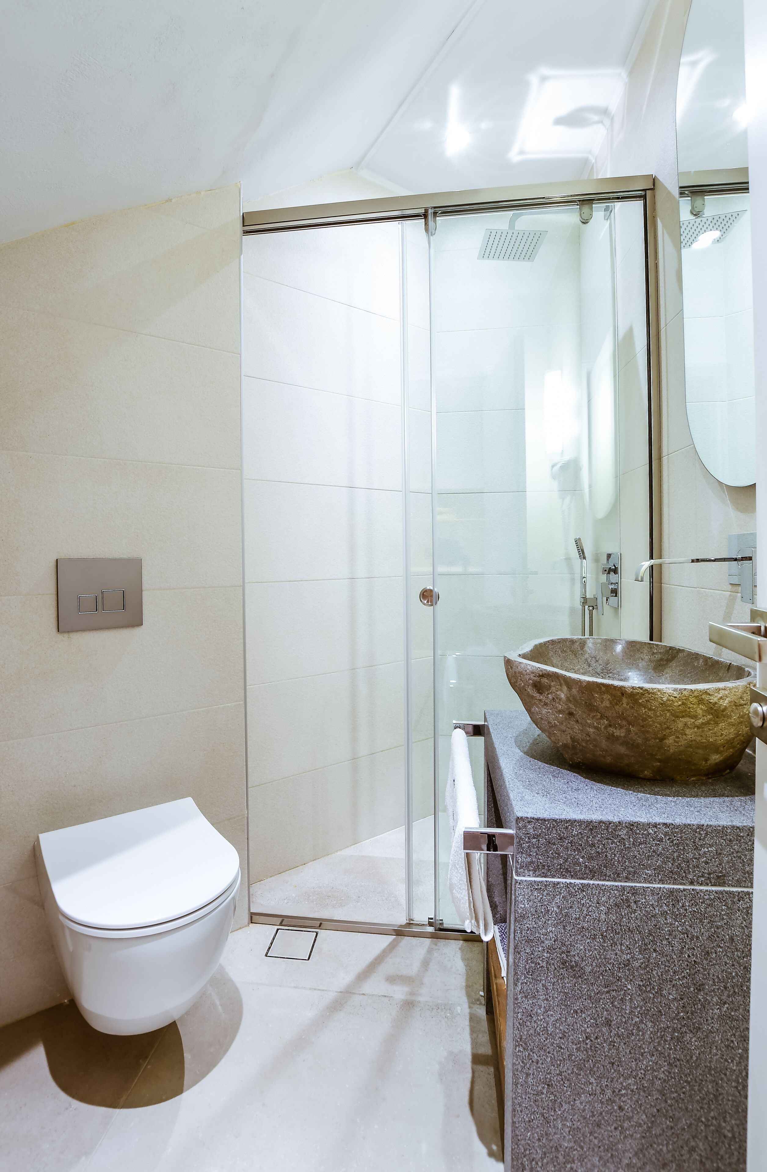 Un baño moderno con cabina de ducha de vidrio, un lavamanos de piedra grande y un inodoro blanco.