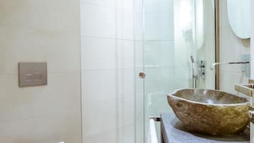 Een moderne badkamer met een glazen douchecabine, een ruime stenen wasbak en een wit toilet.