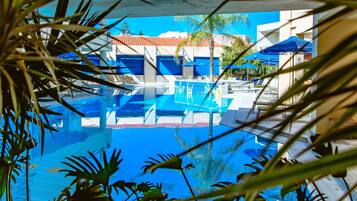 A clear view of a swimming pool with lounge chairs and umbrellas, surrounded by palm trees and buildings.