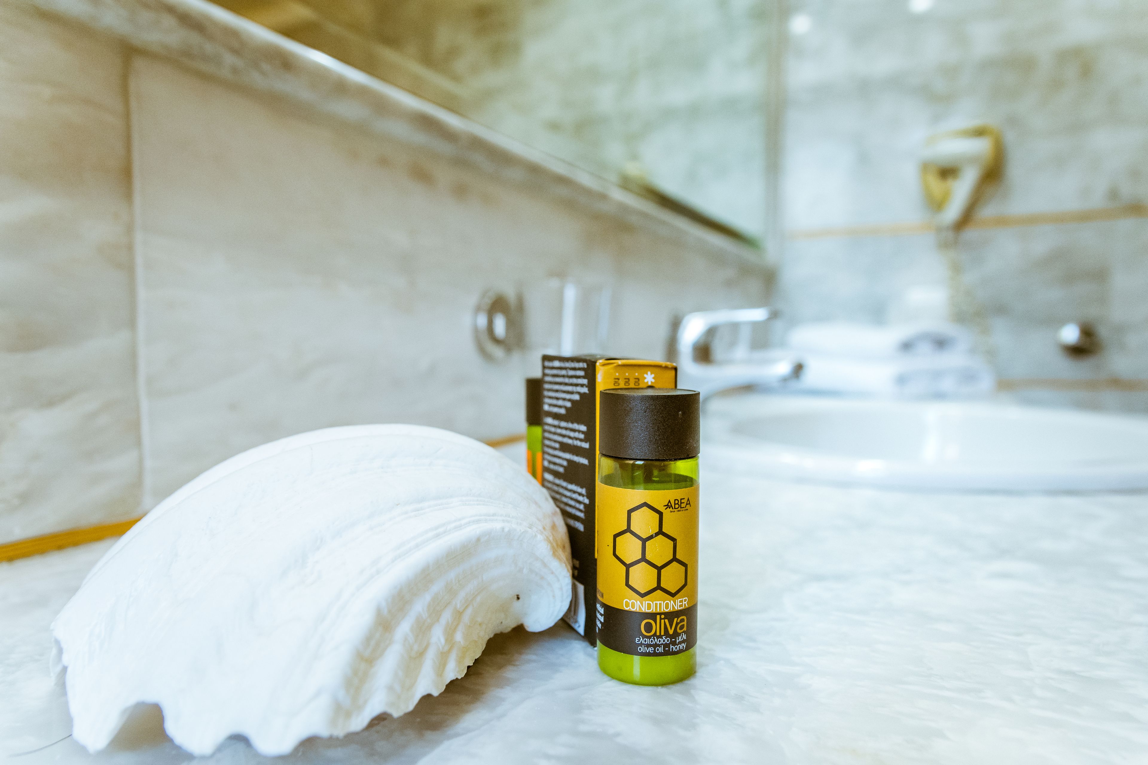 A bathroom with a marble sink, a white towel, and a bottle of olive oil conditioner.