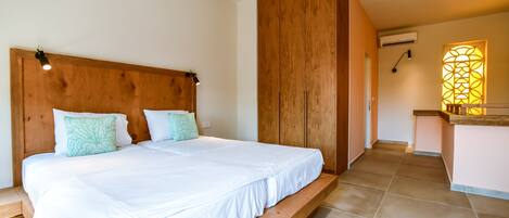 A bedroom with a wooden headboard, a large bed with white bedding, and a small bathroom with a wooden counter and a window.