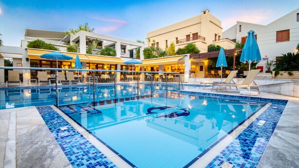 A swimming pool with clear water, surrounded by lounge chairs and umbrellas, and adjacent to a building with outdoor seating. - Anais Collection Hotels & Suites by GHH (Chania)