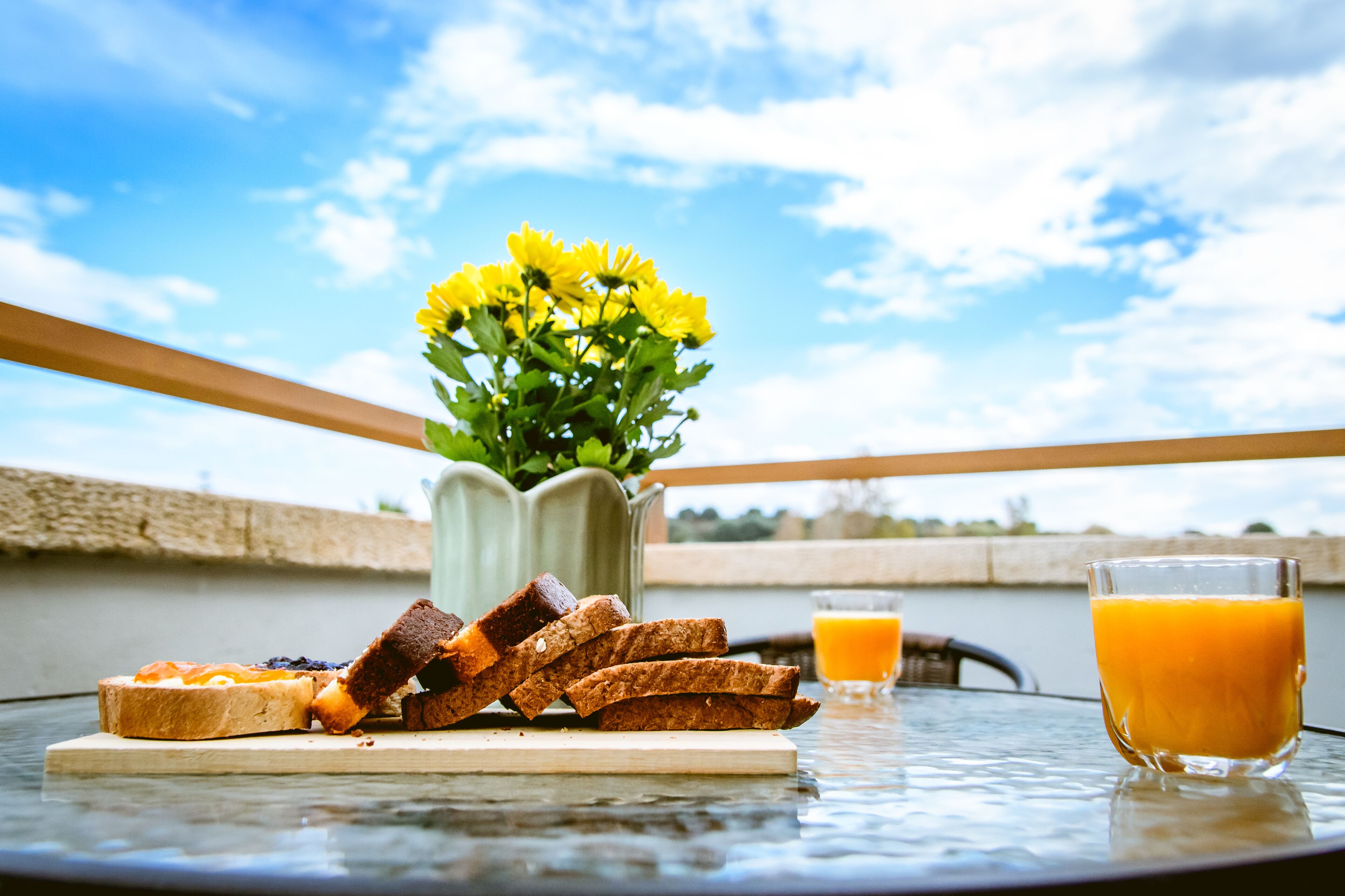 A table with toast, a glass of orange juice, and a vase of yellow flowers.
