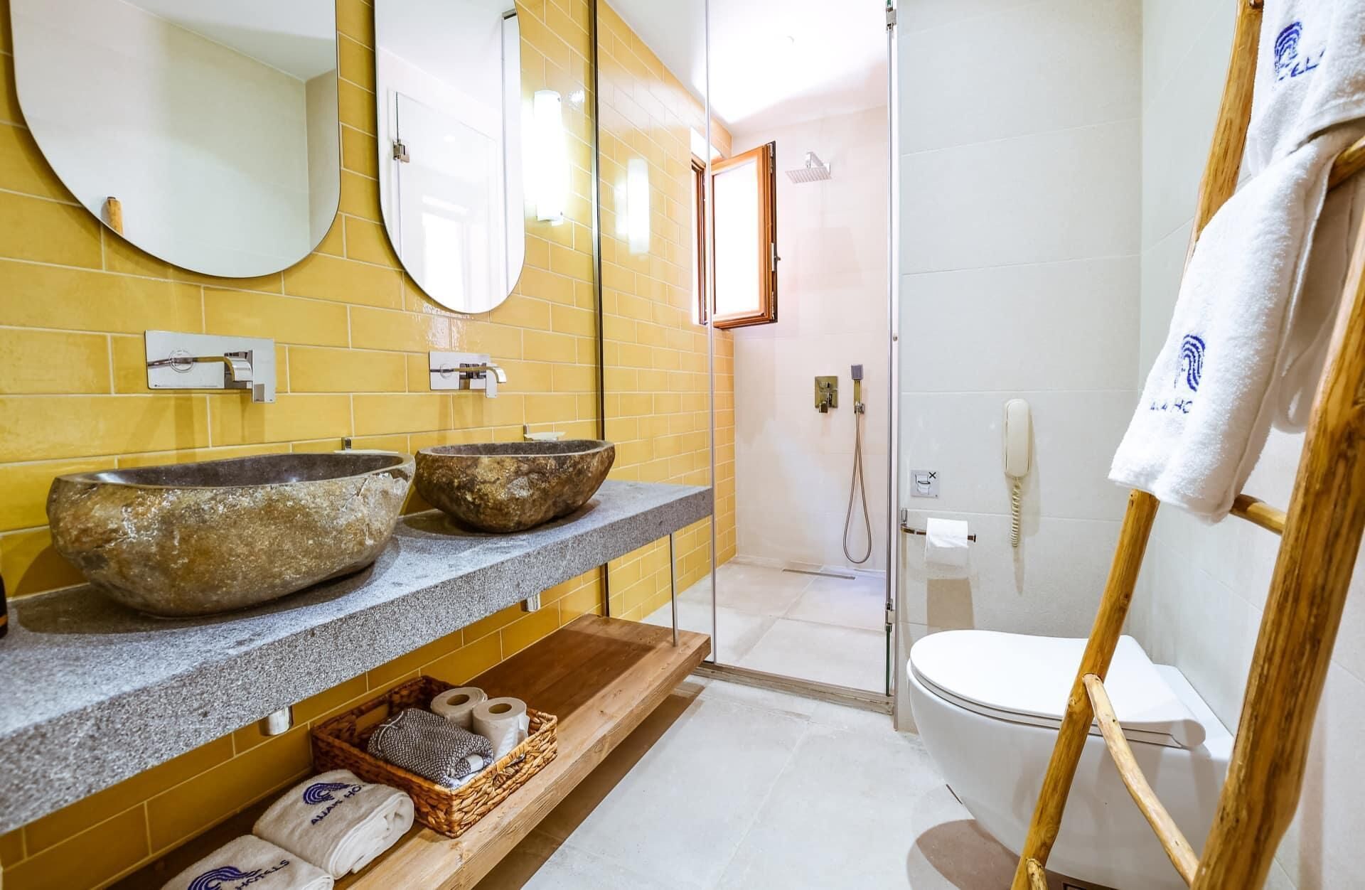 Un baño con dos lavamanos de piedra, un estante de madera con toallas, un espejo y una zona de ducha.