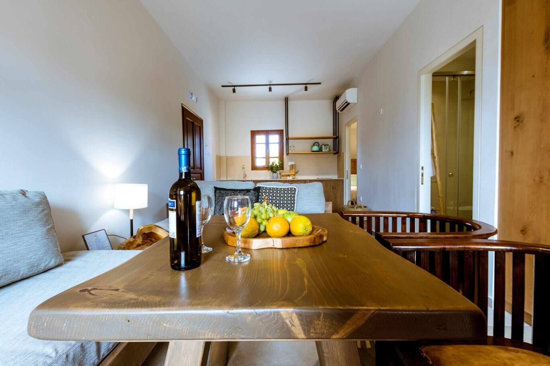 A dining area with a wooden table, a bottle of wine, and a fruit bowl.