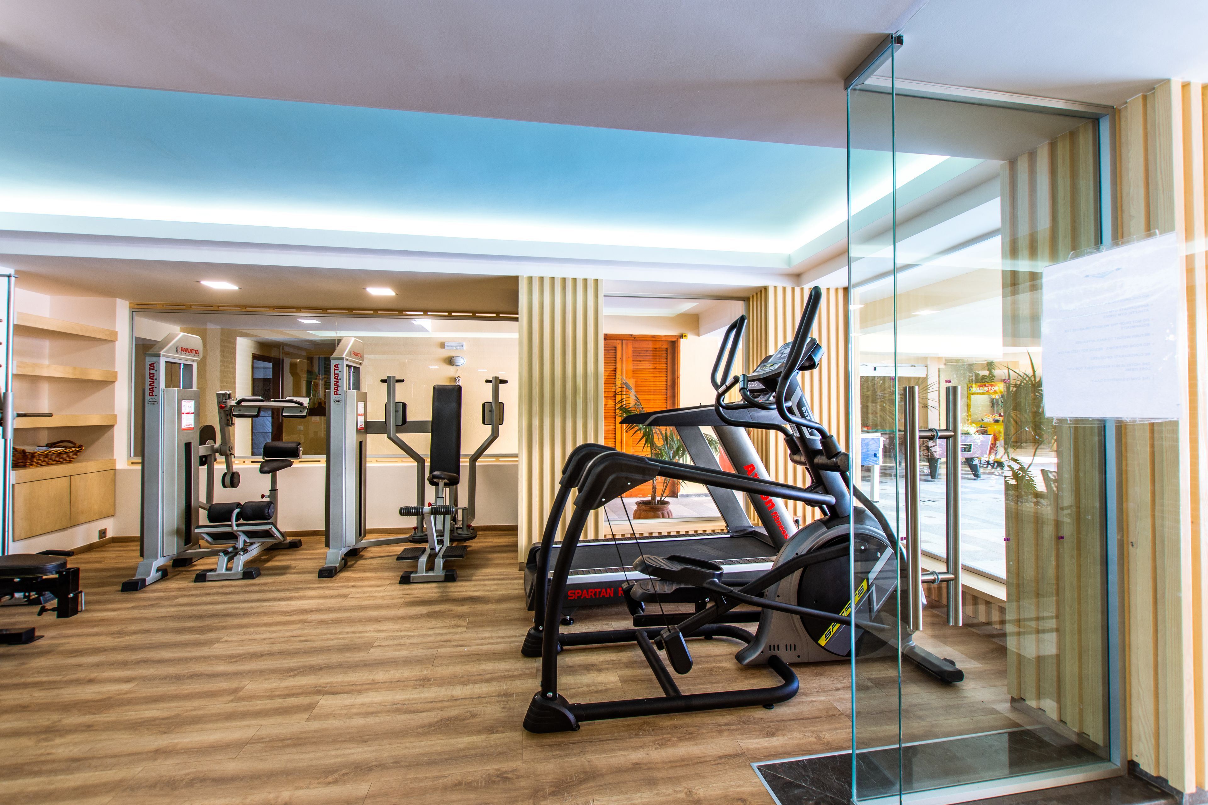 Un gimnasio moderno con diverso equipo de ejercicio, incluyendo cintas de correr y máquinas de pesas, y suelo de madera.