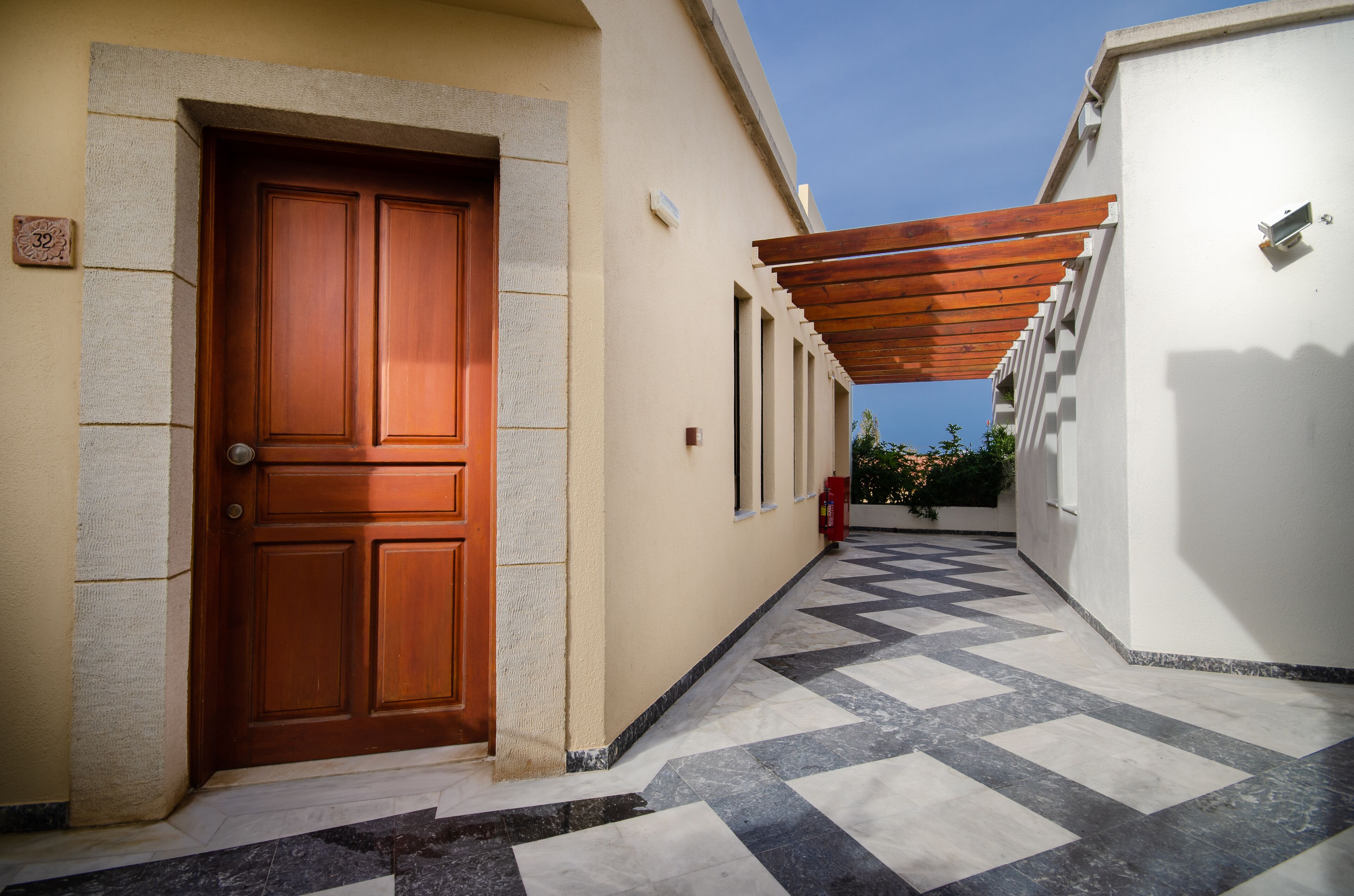 A corridor with a wooden door, tiled flooring, and a pergola structure.