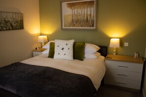 A neatly made bed with a white and green pillow, a dark throw blanket, and two bedside lamps on wooden nightstands.