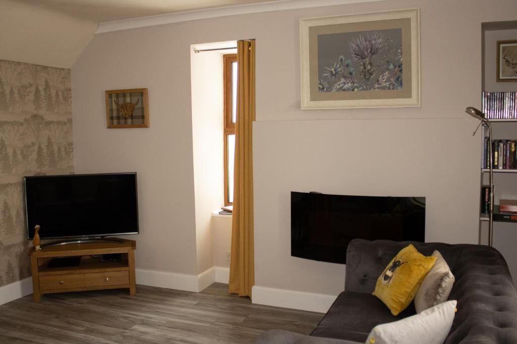 Una sala de estar con un televisor de pantalla plana sobre un soporte de madera, un sofá gris con un cojín amarillo y un cuadro en la pared.