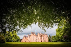 A large, historic building with a symmetrical facade, surrounded by lush greenery and a well-maintained lawn.