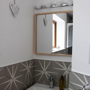 A bathroom with a mirror, a heart-shaped decoration, and a geometric tile backsplash.