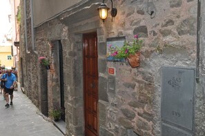 A narrow stone building with a wooden door, potted plants, and a sign indicating a gas meter. - Sandra Villa Rooms (Vernazza)