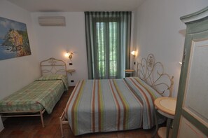 A bedroom with two beds, a window with curtains, a painting on the wall, and a small table with a chair. - Sandra Villa Rooms (Vernazza)