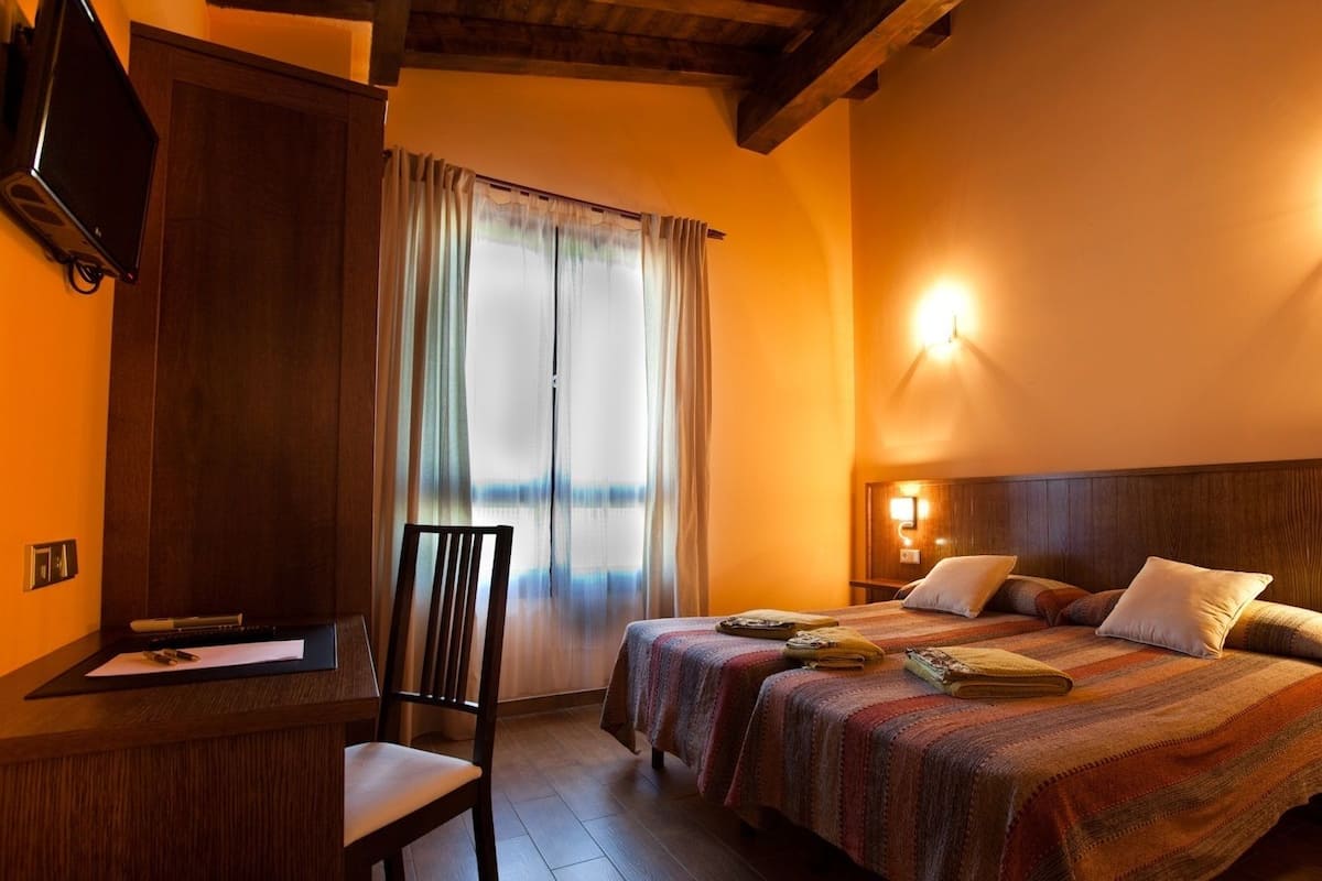 A hotel room with two beds, a desk, a chair, and a large window with curtains.