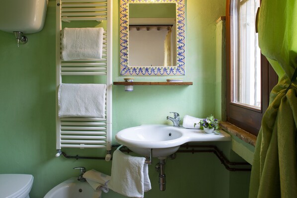 Un baño con lavamanos blanco, un espejo con marco decorativo, un perchero y una ventana con cortina verde.