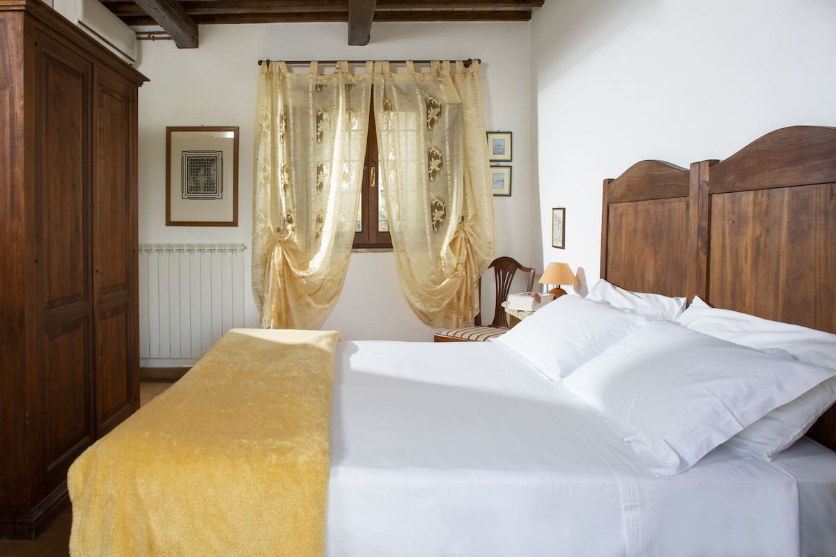 A bedroom with a bed, wooden headboard, and a window with curtains.