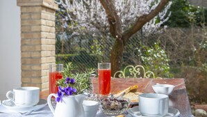A breakfast setup with a table, cups, a pitcher, and a glass of red drink, set against a brick wall and a tree with white blossoms. - B&B With Pool and View of Assisi (Assisi)