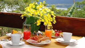 Ein Esstisch mit Seeblick, ein Strauß gelber Blumen und eine Auswahl an Speisen und Getränken.