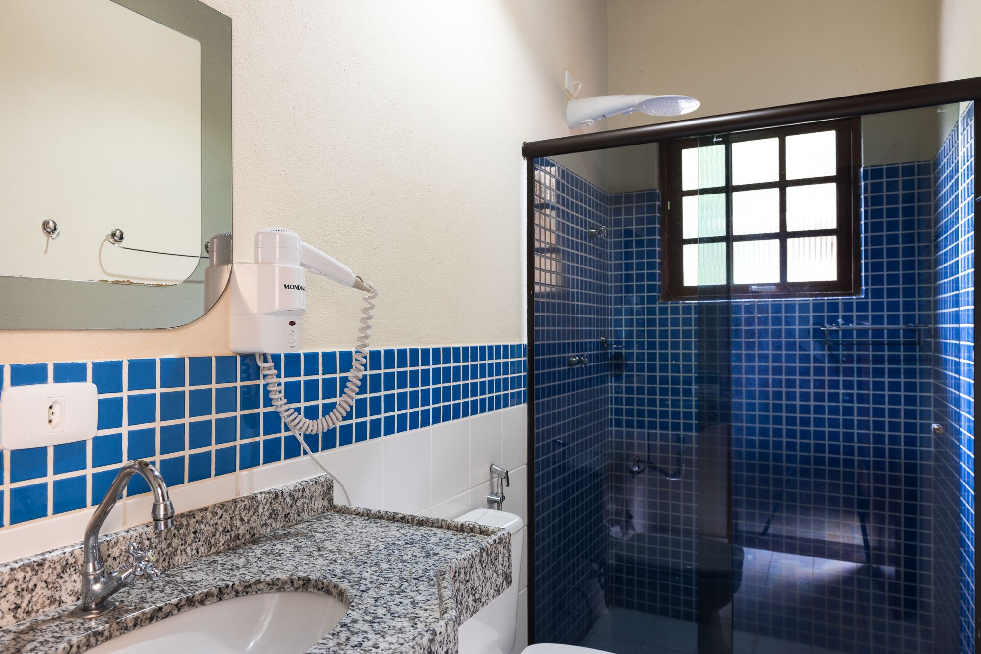 Een badkamer met een wastafel, spiegel, haardroger en een douchegedeelte met blauwe tegels.