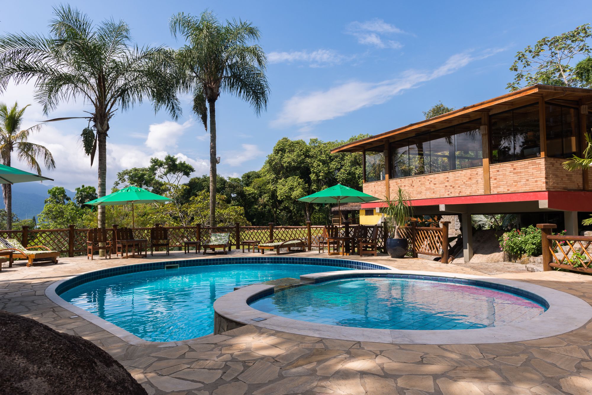 A pool area with two swimming pools, wooden deck chairs, and umbrellas.