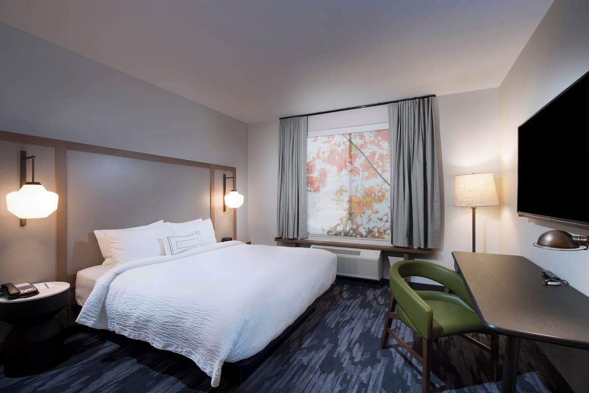 A hotel room with a bed, a desk, a chair, a telephone, and a window with curtains.