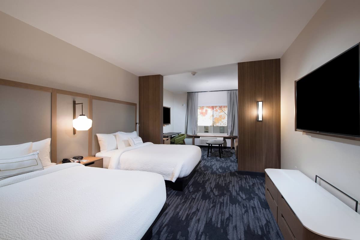 A hotel room with two beds, a desk, a TV, and a window with curtains.