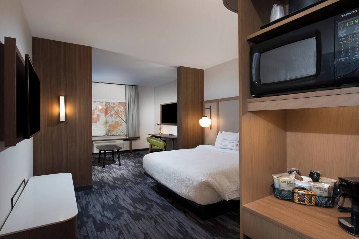 A hotel room with a bed, a desk, a chair, a microwave, and a coffee maker.