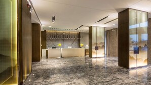 Un hall d’hôtel moderne avec un comptoir d’accueil, des panneaux muraux décoratifs et un sol en marbre.