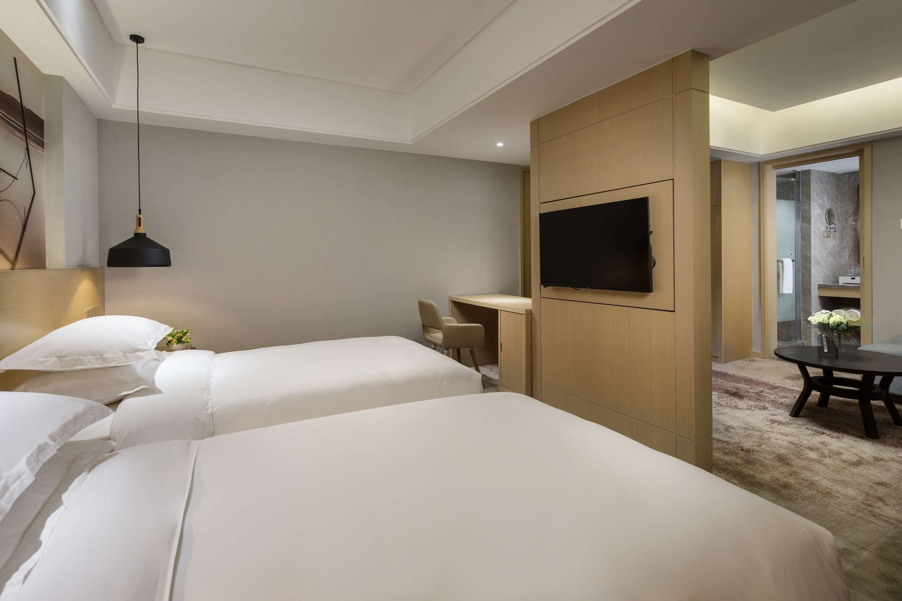 A hotel room with two beds, a desk, a TV, and a dining area.