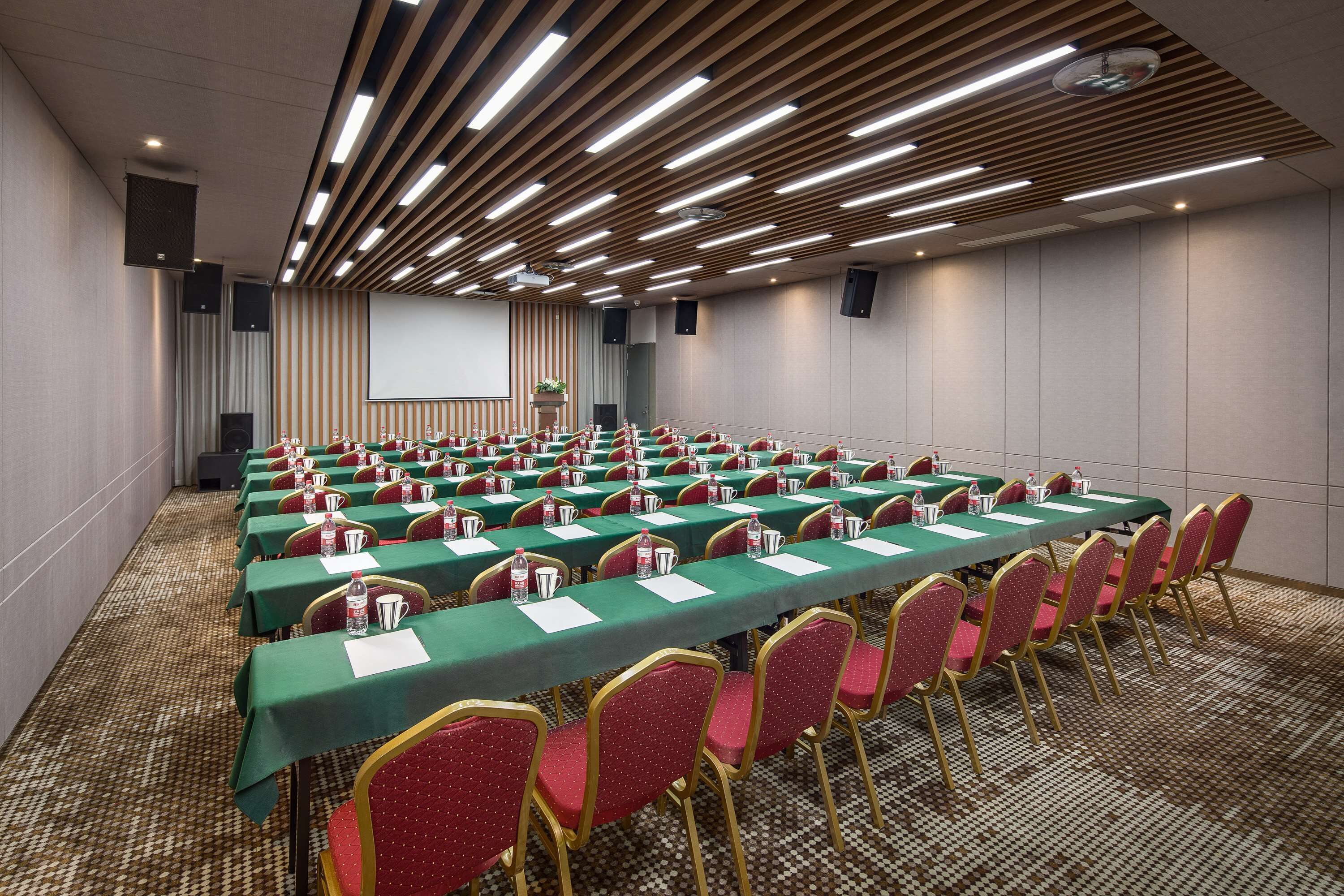 A conference room with rows of tables and chairs, equipped with microphones and projectors.