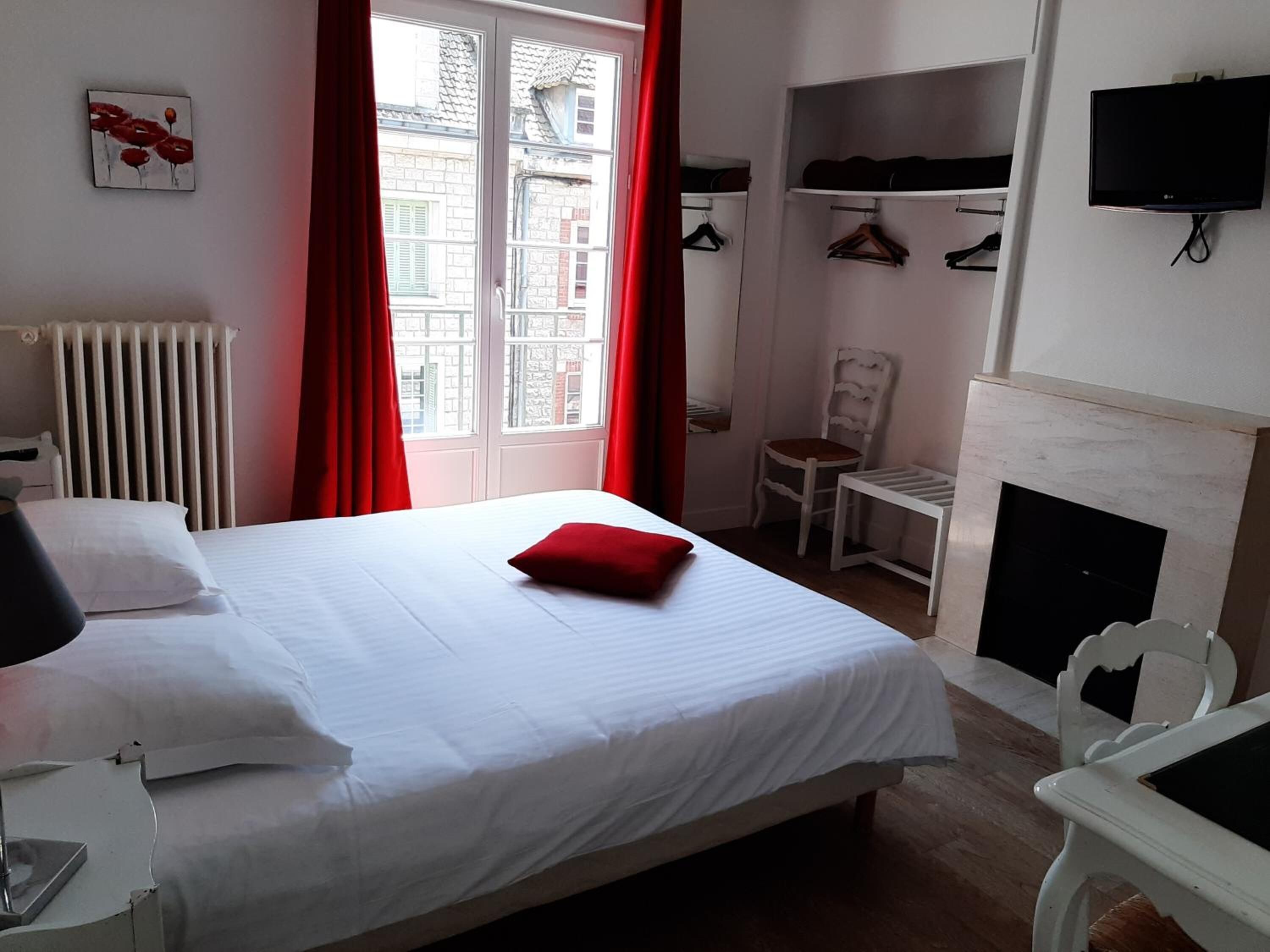 A hotel room with a bed, a chair, a TV, a fireplace, and a window with red curtains.