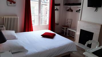 A hotel room with a bed, a chair, a TV, a fireplace, and a window with red curtains.