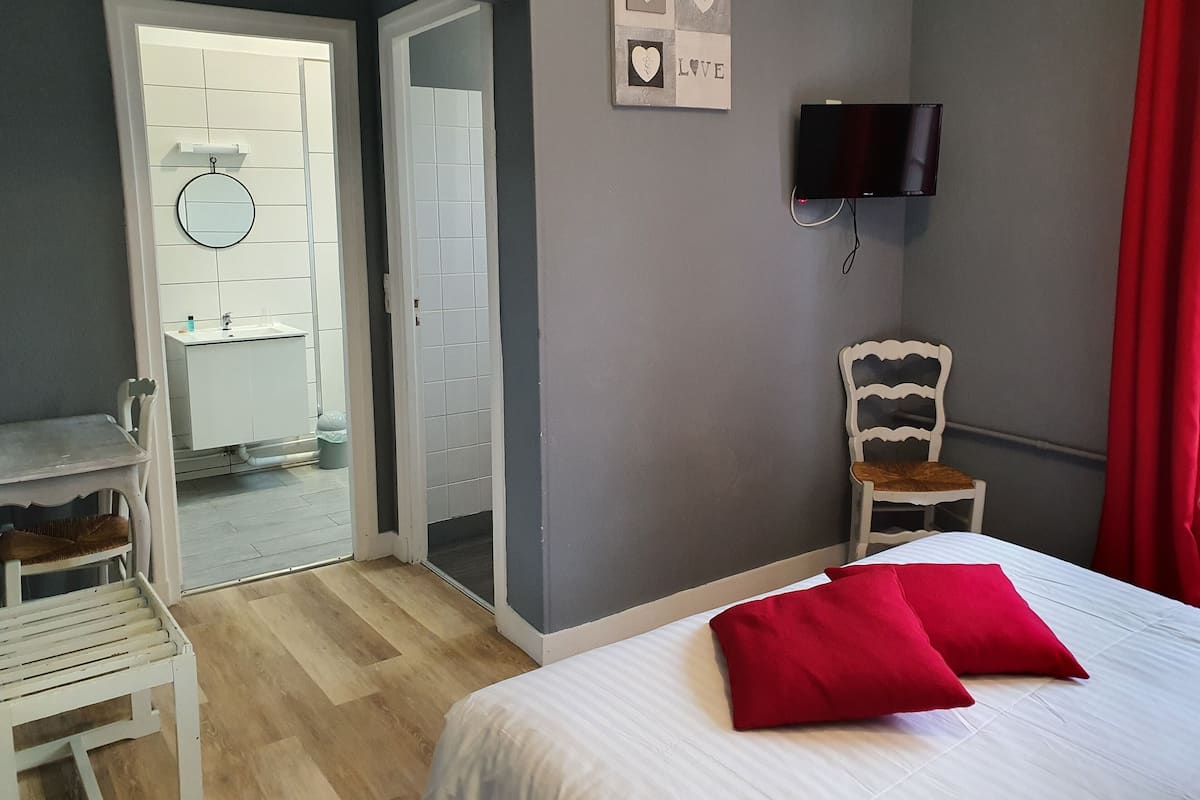 A bedroom with a bed, a chair, a television, and a bathroom visible through an open door.