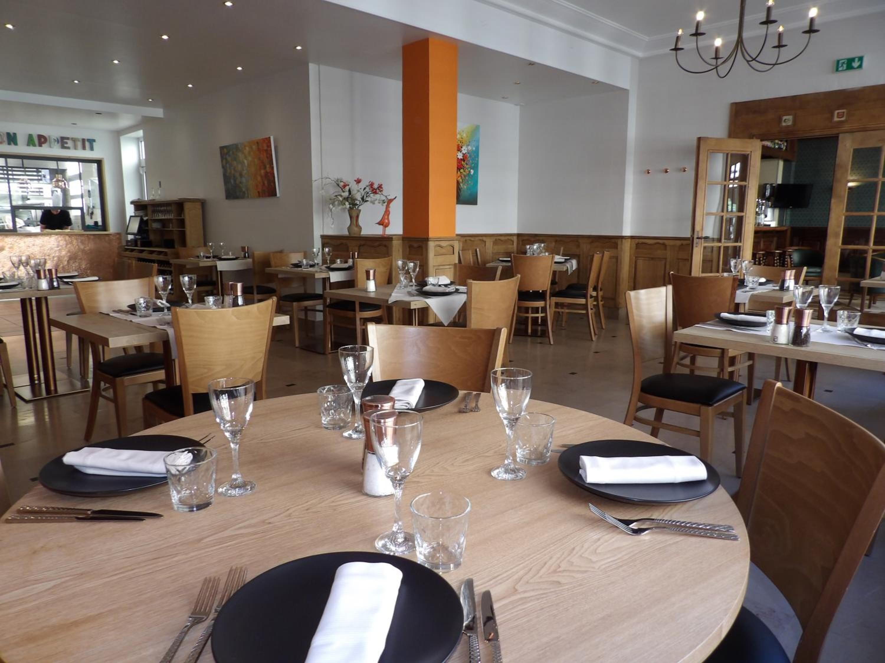 En restaurang med runda bord, dukade för middag, med svarta tallrikar, vita servetter och klara glas.