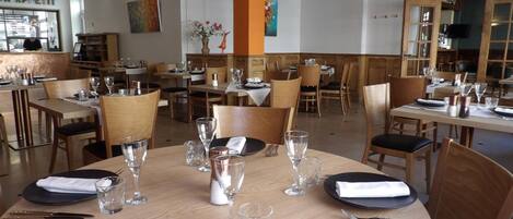 Un restaurant avec des tables rondes dressées pour le dîner, où l’on utilise des assiettes noires, des serviettes blanches et des verres transparents.