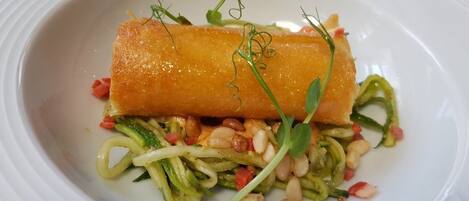 A dish with a golden-brown item on top, green vegetables, and pine nuts.