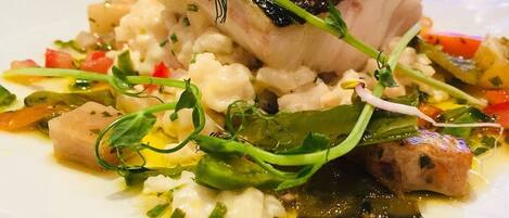 A white plate with a fish dish, vegetables, and a garnish.