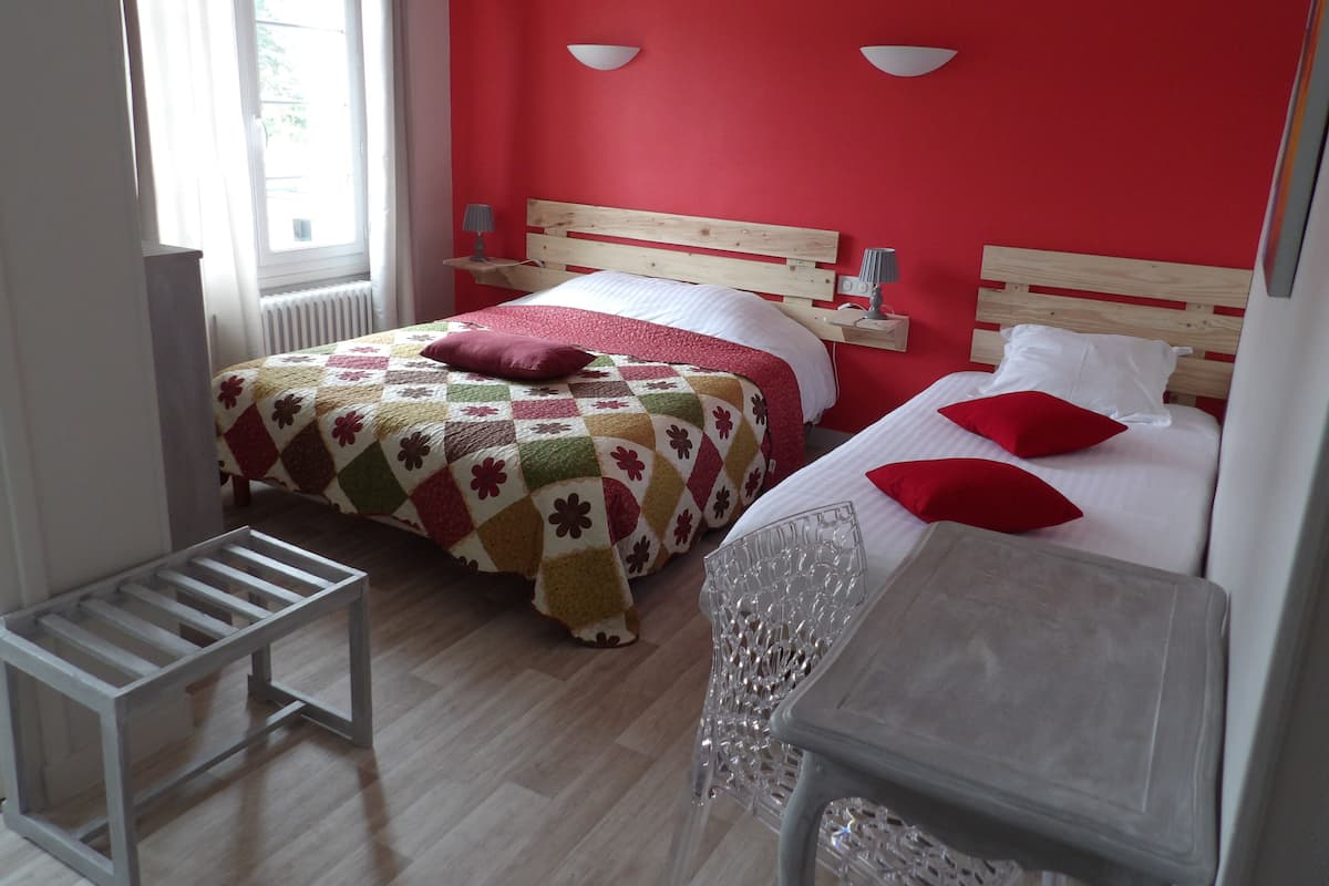 A bedroom with two beds, a wooden headboard, a radiator, a window with curtains, and a bedside table with a lamp.