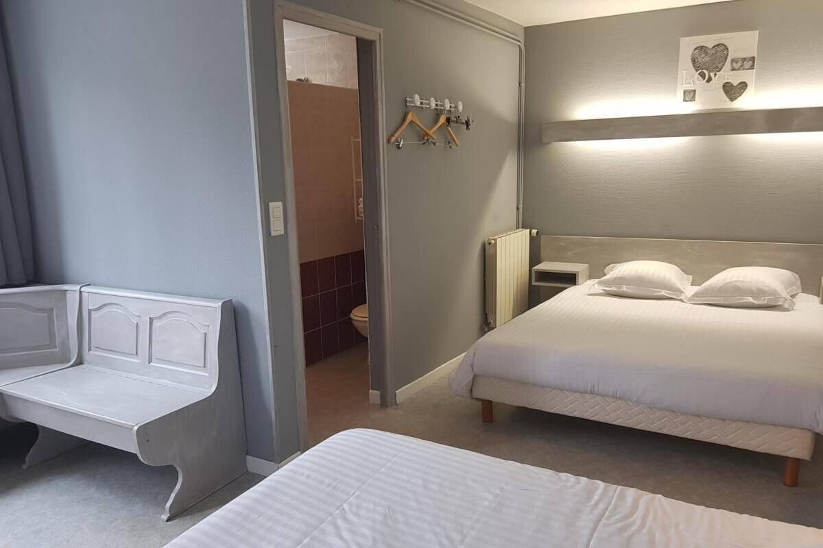 A hotel room with a bed, a bench, a radiator, and a wall-mounted coat rack.