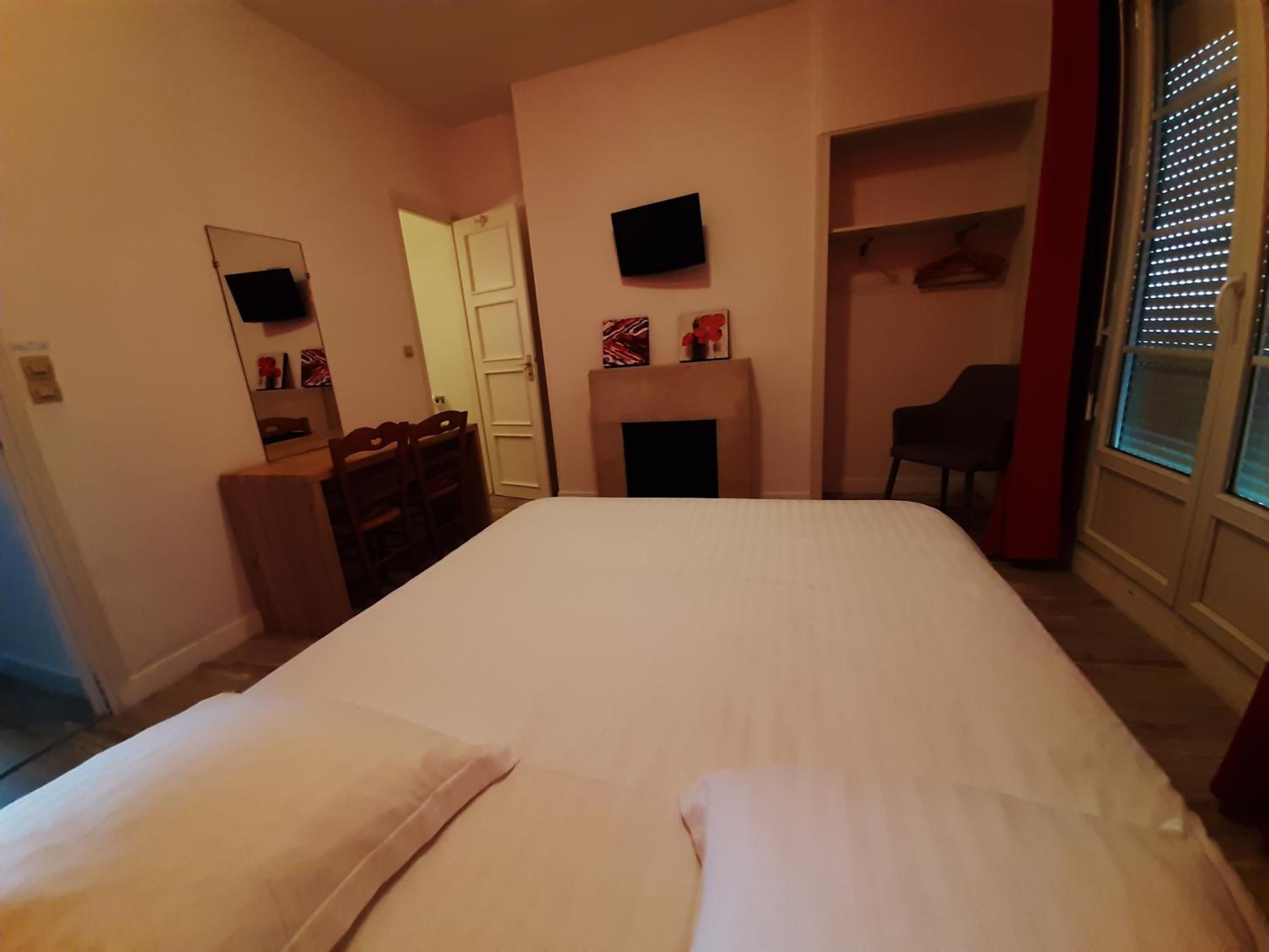 A bedroom with a bed, a dresser, a chair, a TV, and a fireplace.