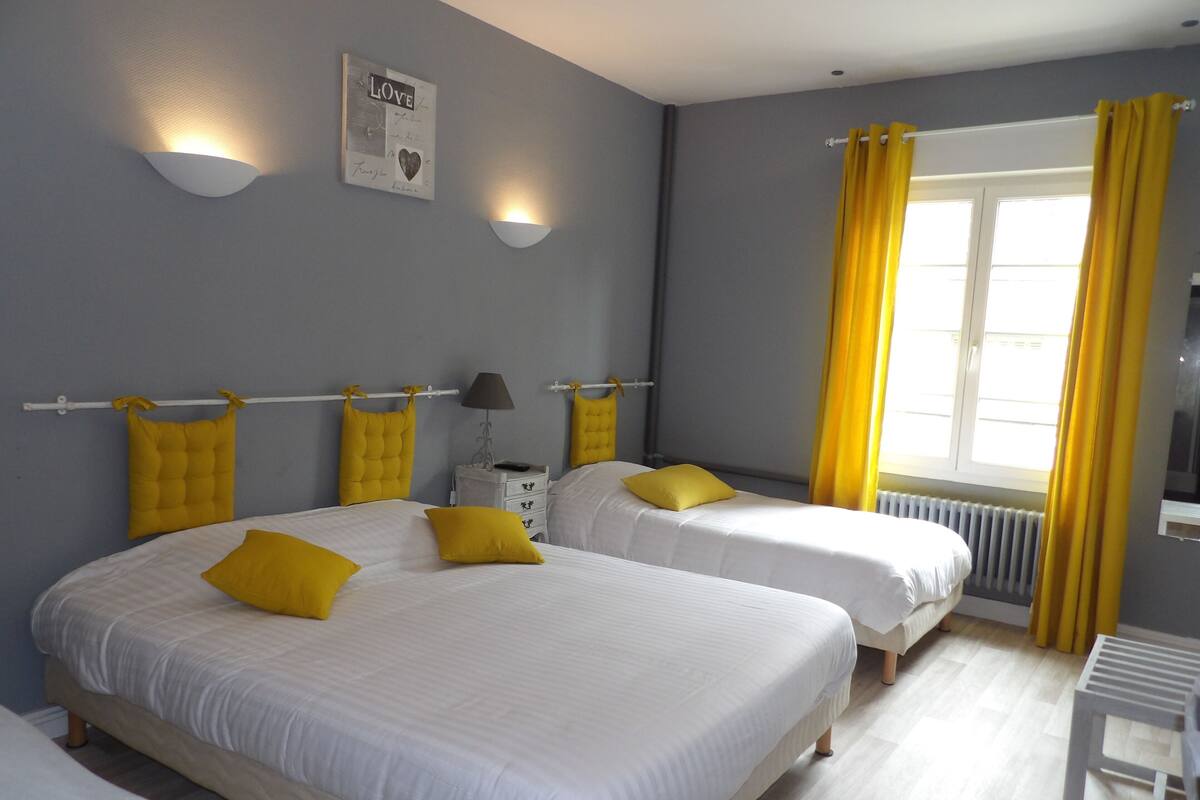 A hotel room with two beds, each with a headboard and a bedside table with a lamp.